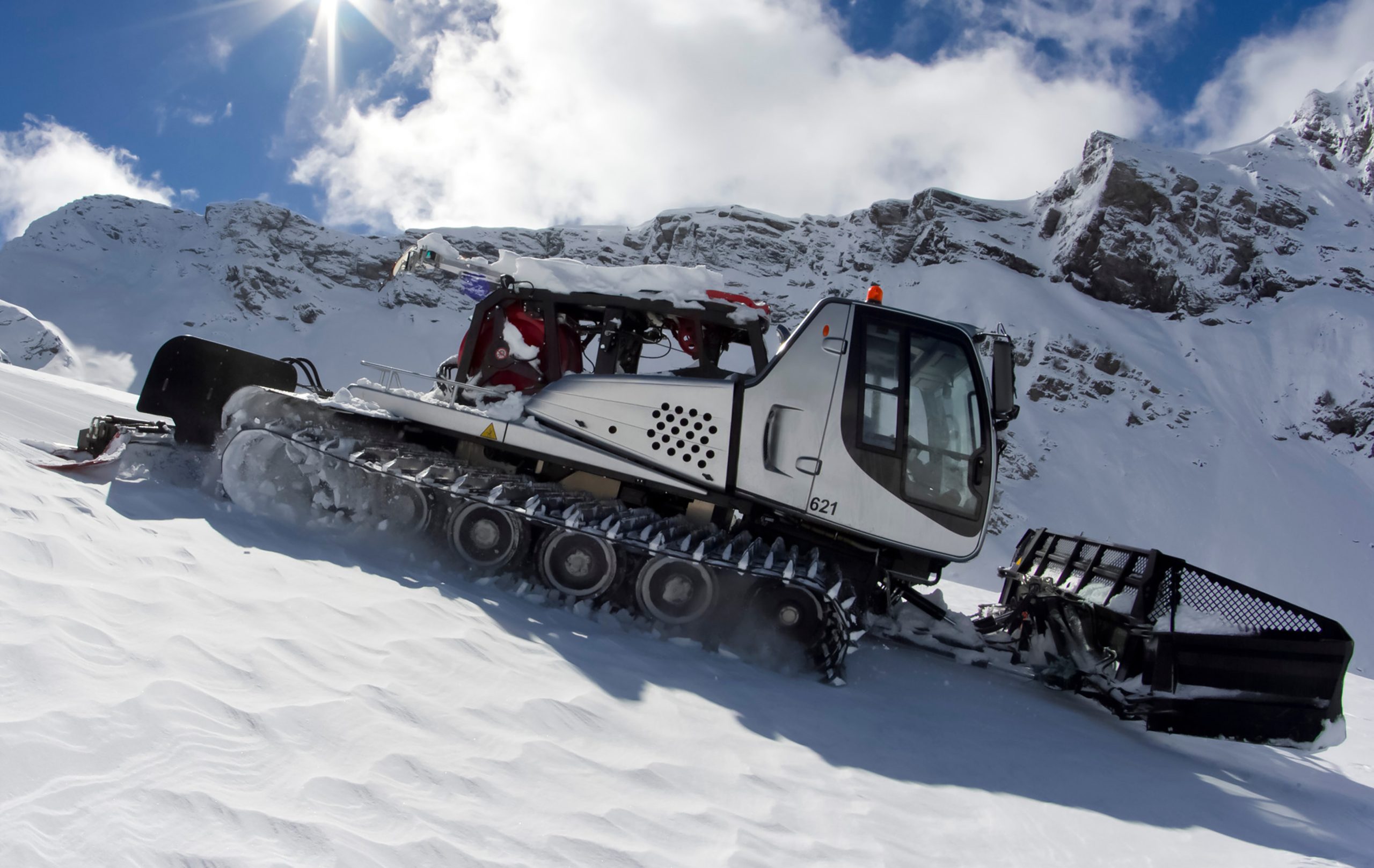 Ratrak, grooming machine, special snow vehicle Schneeraupe, die in der Sonne auf einem beschneiten Hang fährt und Tieftemperaturschmierfette nutzt, um leichtläufig zu bleiben
