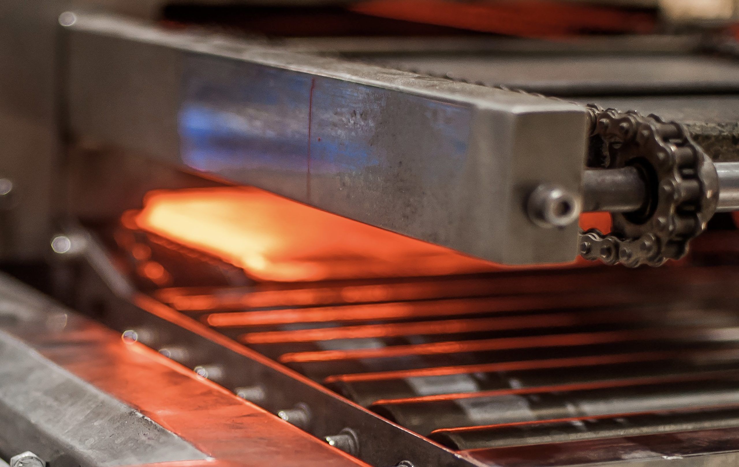 Ein kettengetriebenes Förderband, das ein Metallprodukt aus einem Schacht fährt, in dem glühend heiße Temperaturen herrschen und deswegen Hochtemperatur Kettenöle verwendet werden müssen